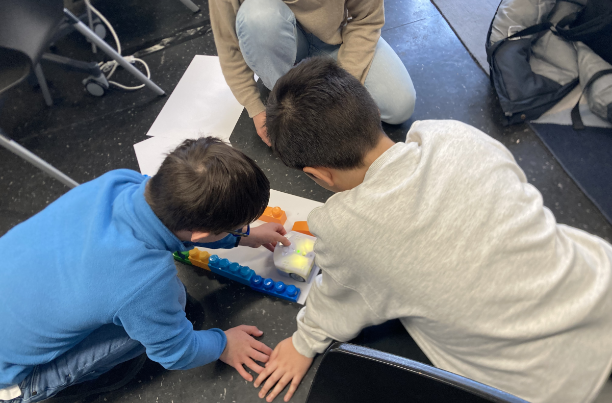 photo of two children sitting on the floor, working with a robot