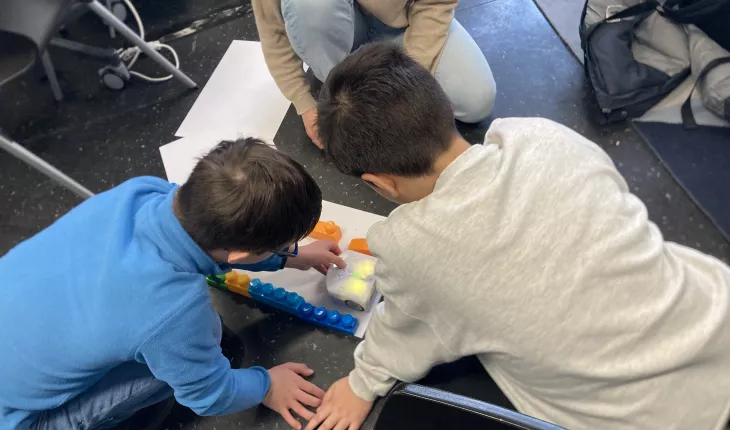 photo of two children sitting on the floor, working with a robot