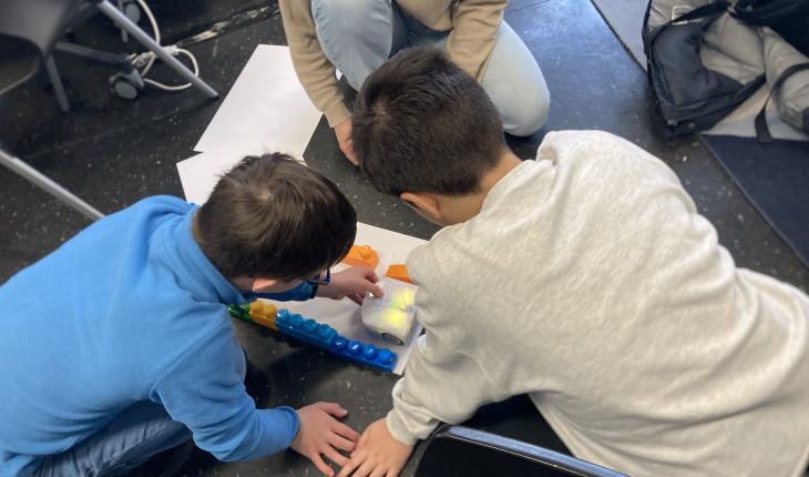 photo of two children sitting on the floor, working with a robot